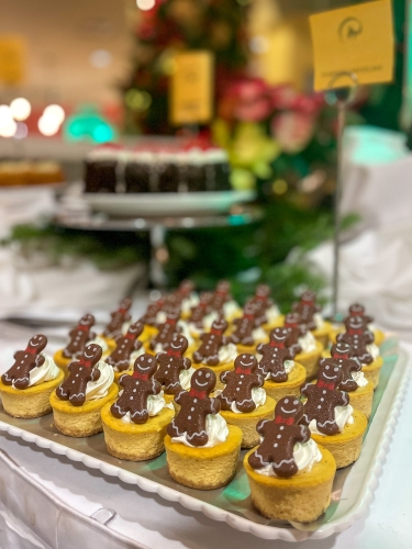 A serving tray on a Christmas buffet table with mini cheesecakes topped with whipped cream and miniature gingerbread men. 