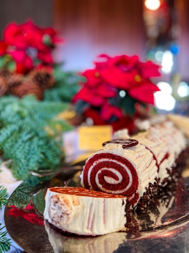 A beautiful red velvet yule log set amidst red poinsettias on a Christmas buffet table.