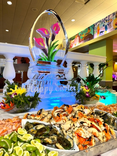 A large ice sculpture with pink lilies and the words "Happy Easter" sits behind an array of fresh seafood. 