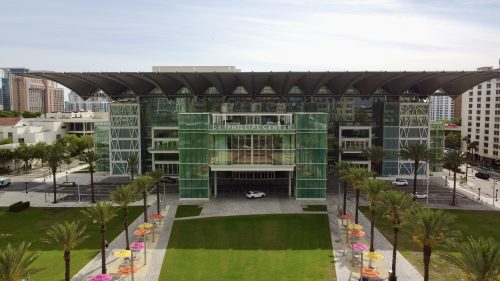 A photo of the Dr. Phillips Center, a great place to unwind in Orlando, showing its large building with a lawn and palm trees lining the entrance.