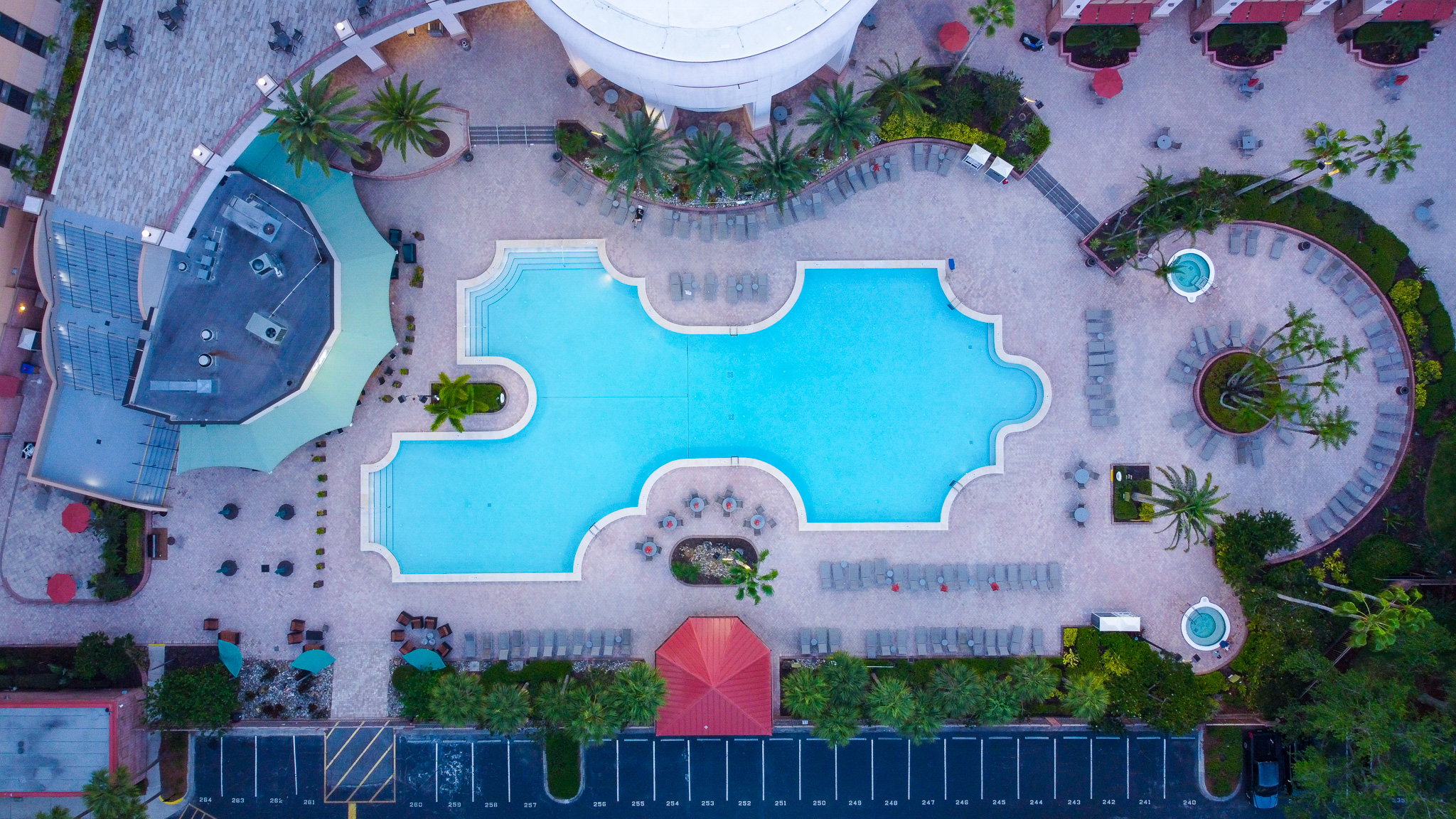 An aerial view of the pool deck at Rosen Centre showing a sizeable swimming pool, two hot tubs, and the roof of Harry's Poolside Bar & Grill.