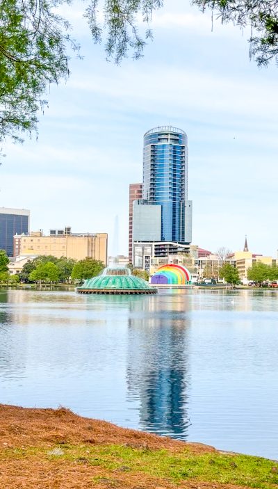 A body of water with a fountain and a tall building in the background among smaller buildings. This is Lake Eola, a great place to unwind in Orlando.