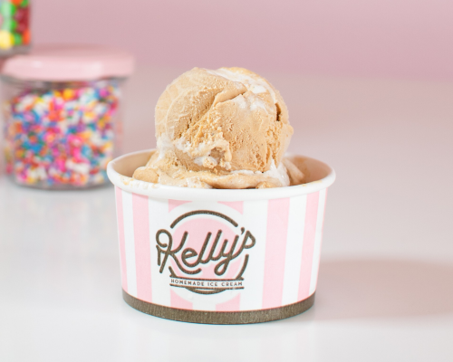 A scoop of pumpkin ice cream in a pink and white paper cup that says "Kelly's homemade ice cream." The perfect treat to satisfy your sweet tooth.