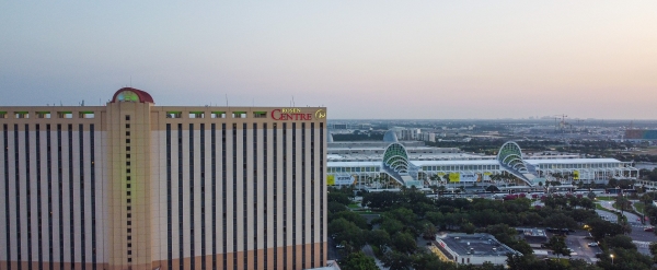 A wide shot photo of a tall hotel sitting adjacent to the large white and glass Orange County Convention Center at dusk. Host your green event at Rosen Centre.