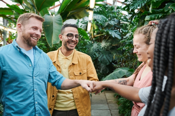 Two men and two women fist-bump in a green space with tropical plants. 